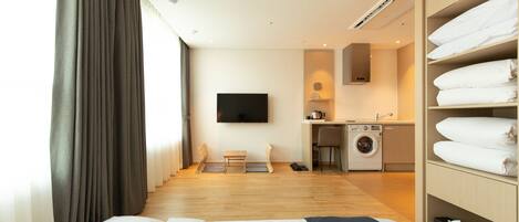 Ein Hotelzimmer mit Bett, Fernseher, Schreibtisch, Waschmaschine und Kleiderschrank.