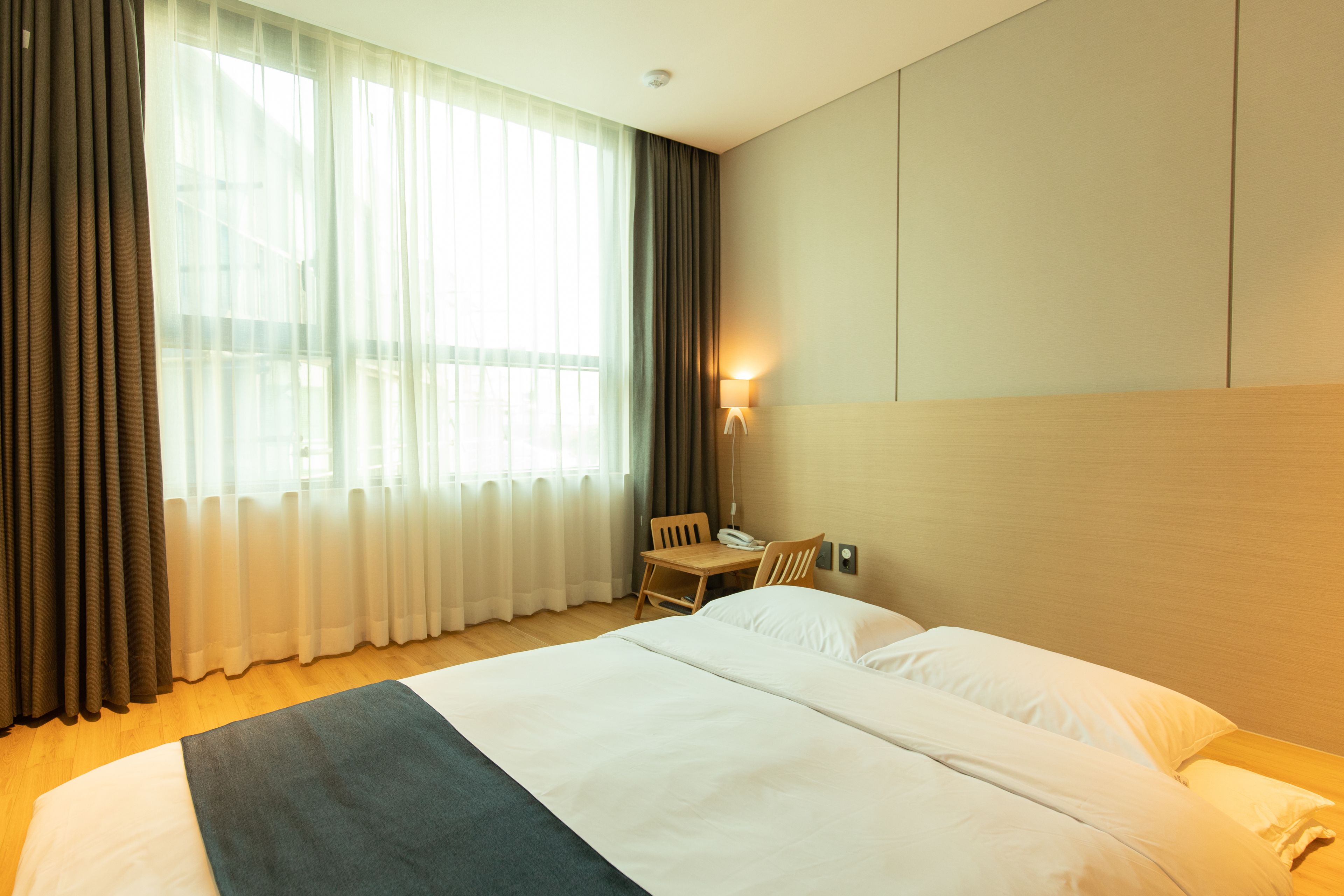 Habitación de hotel con una cama grande, un escritorio con una silla, una lámpara y una ventana con cortinas.
