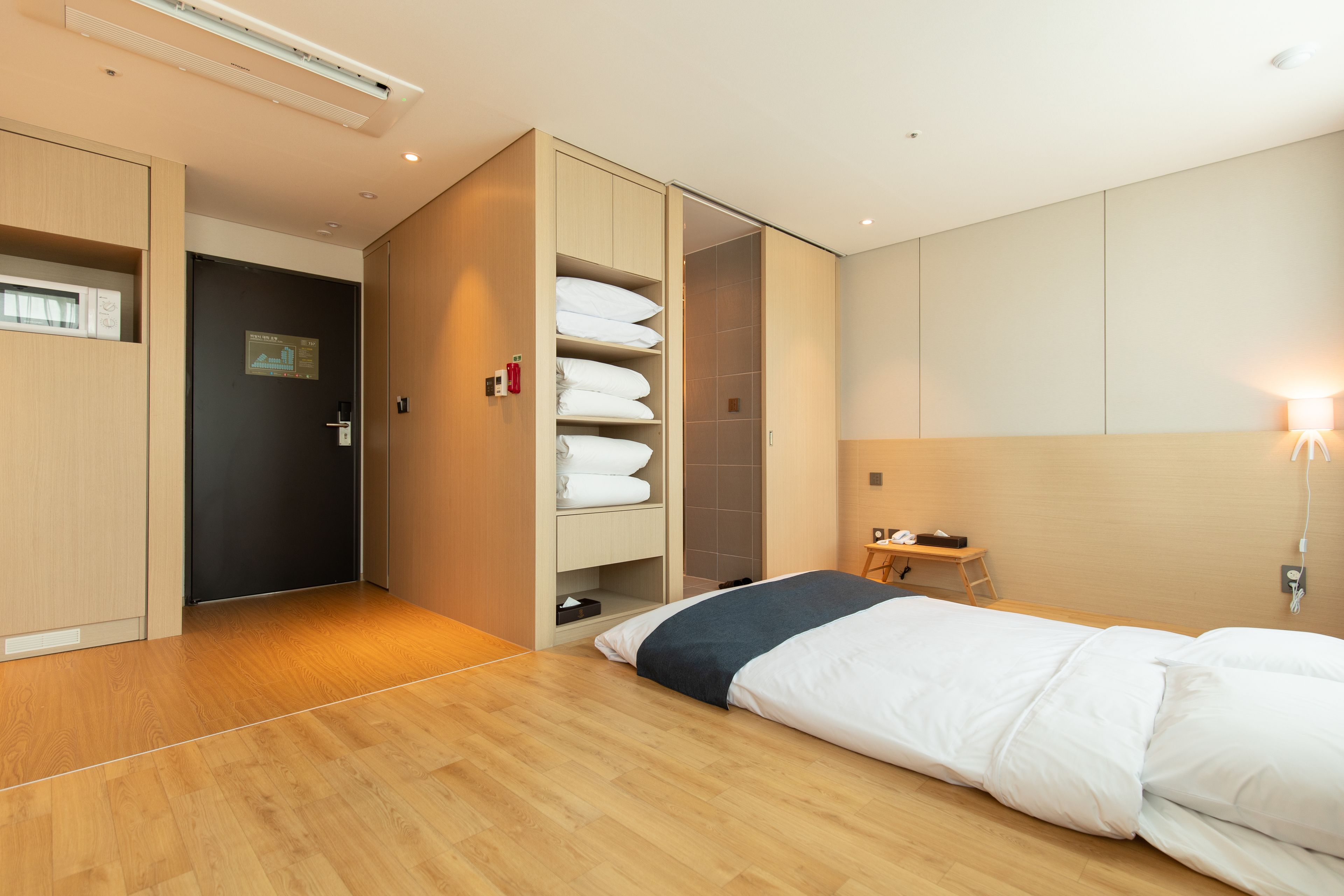 Een moderne hotelkamer met houten vloer, een bed met wit beddengoed, een inbouwkleerkast, een klein bureau en een nachtkastje.