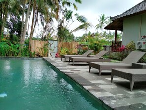 A swimming pool with lounge chairs and a wooden fence. - Amaya Cottage Ubud (Ubud)