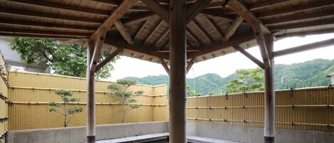 Een traditionele Japanse onsen met stenen vloeren, een houten dak en een bamboebegraaide achtergrond.