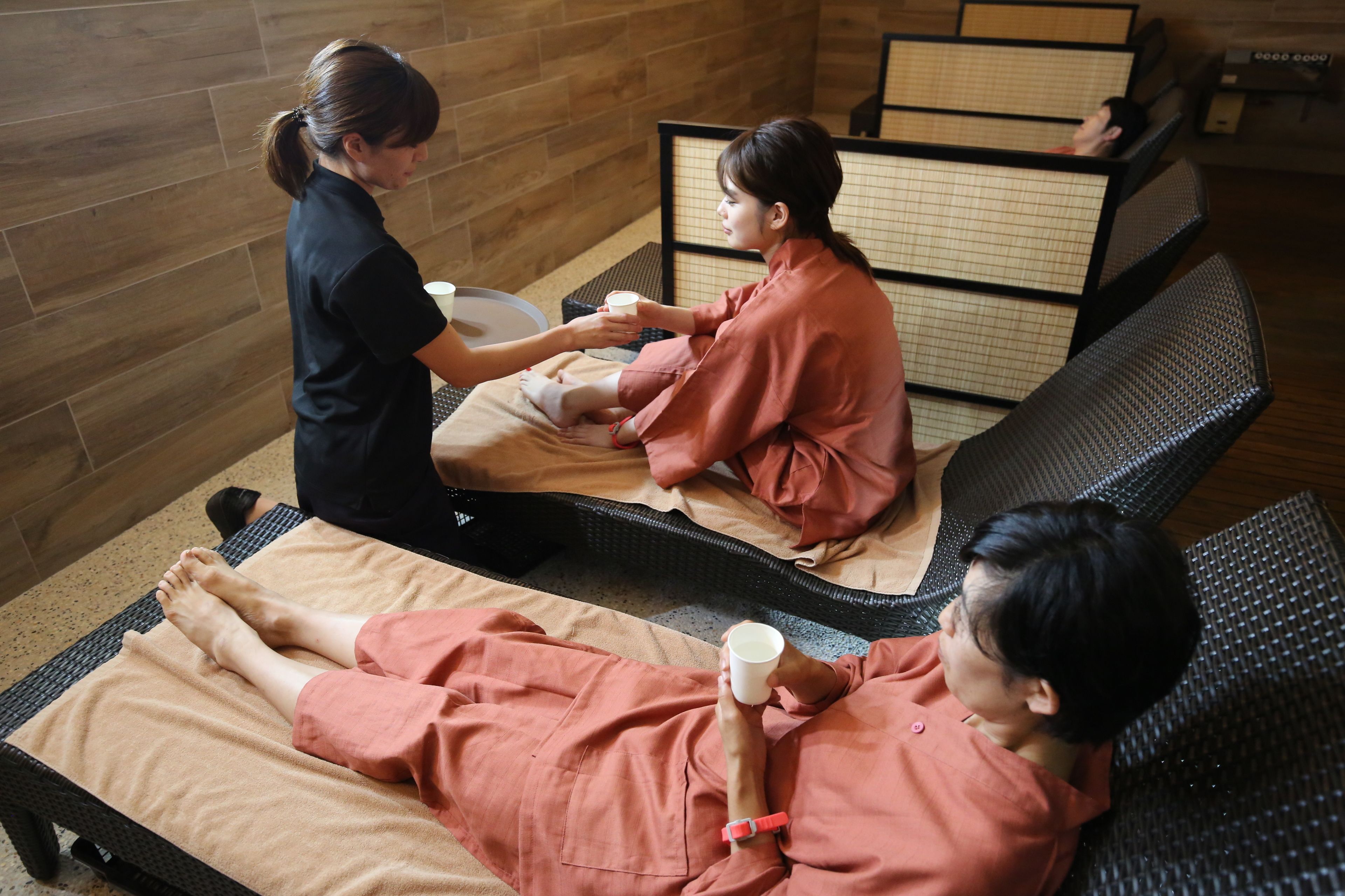A massage therapy room with two massage tables, a wooden wall, and a tatami mat partition.