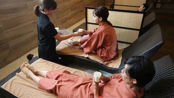 A massage therapy room with two massage tables, a wooden wall, and a tatami mat partition.