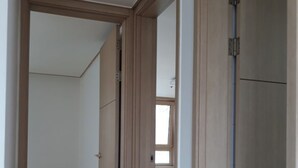 Un pasillo con suelo de madera, una puerta que da a una habitación con ventana y una lámpara de techo a la vista.