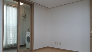 Una habitación con suelo de madera, una puerta corredera de vidrio que da a un área de lavandería y una pared blanca con un interruptor de luz.