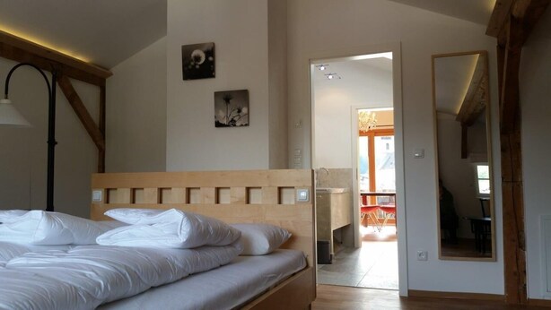 Ein Schlafzimmer mit einem hölzernen Kopfende, einem Bett mit weißen Leinentüchern, einem Nachttisch und einem Spiegel an der Wand.