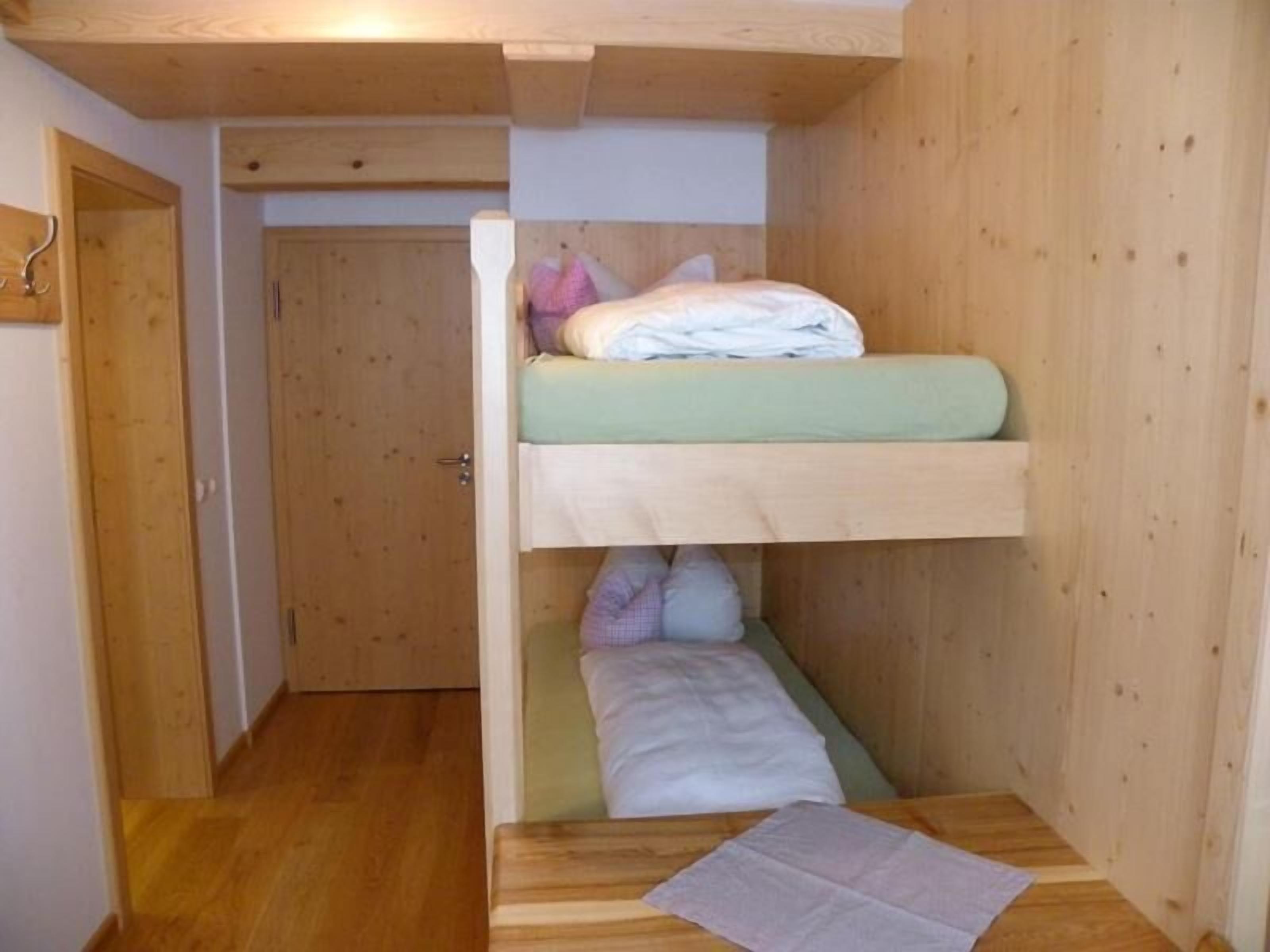 Une petite pièce avec un lit superposé, des murs en bois et une porte donnant sur une autre pièce.