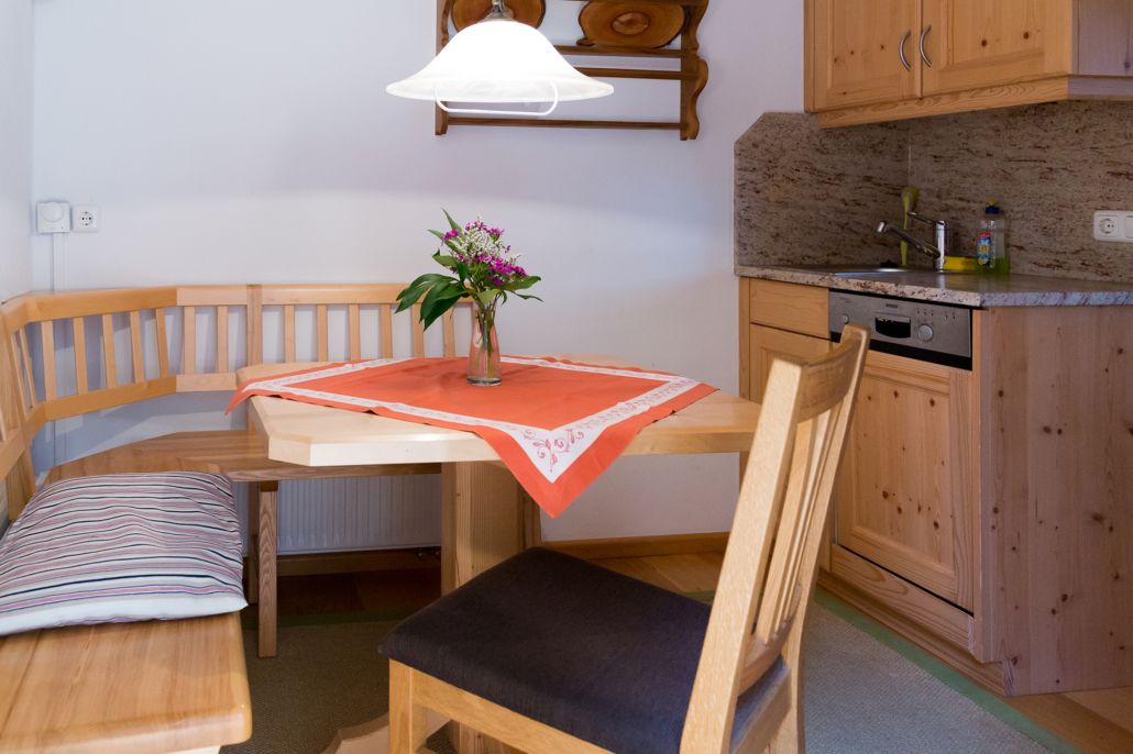A compact kitchen with wooden cabinets, a dining table with a bench, and a small island with a lamp.