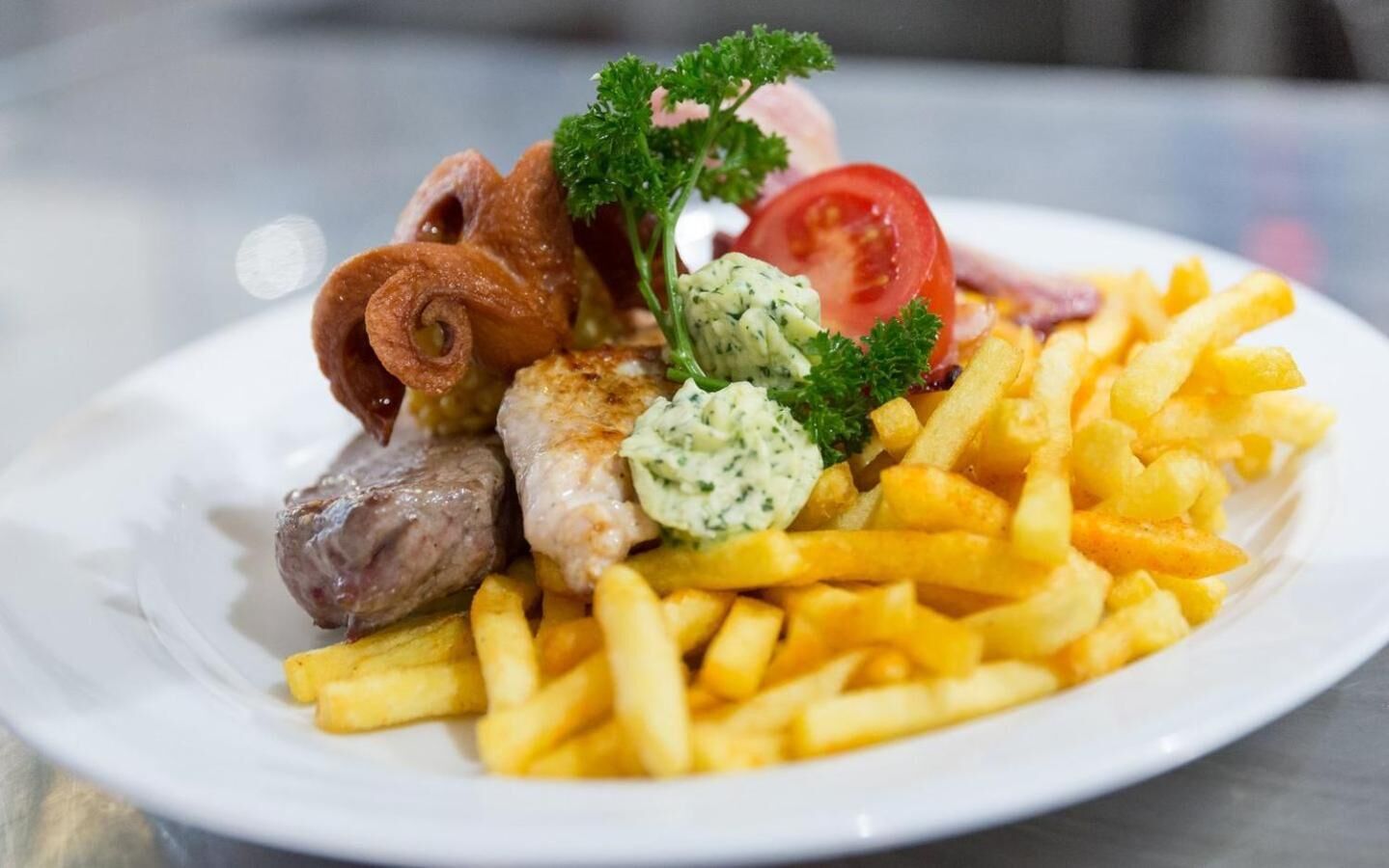 A plate with French fries, a slice of tomato, a piece of meat, and a roll of bacon.