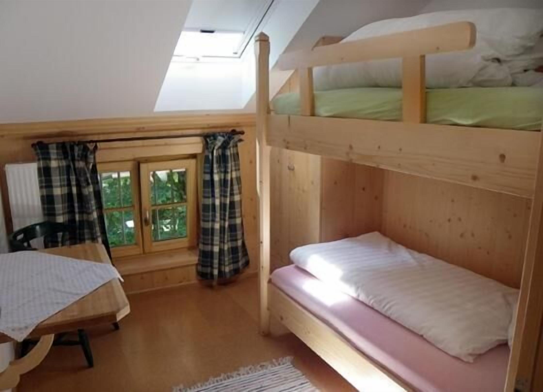 A small, cozy room with a bunk bed, a desk, and a window with curtains.