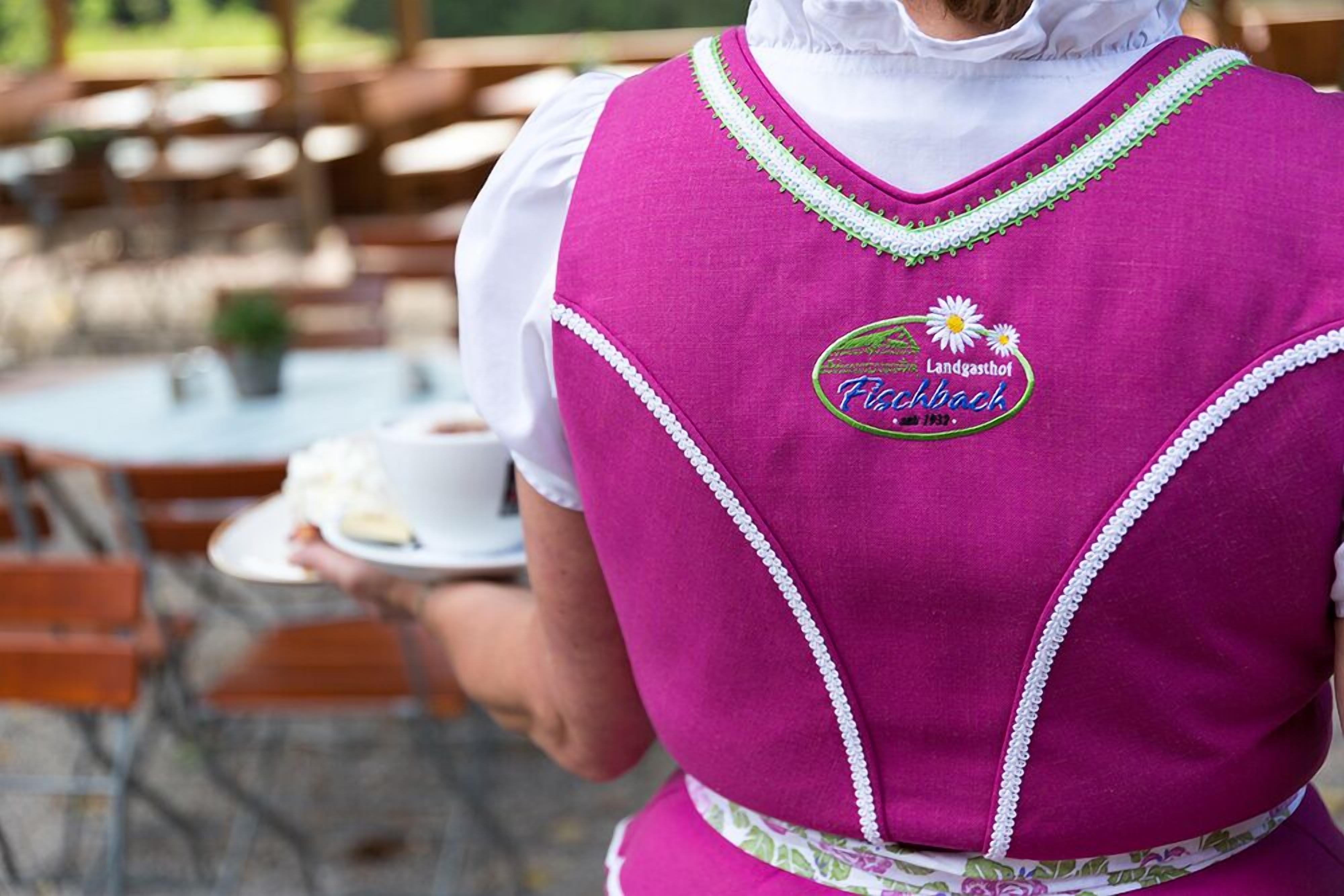 Eine Person in einer rosa Schürze mit einem Logo und Text hält einen Teller mit Essen.