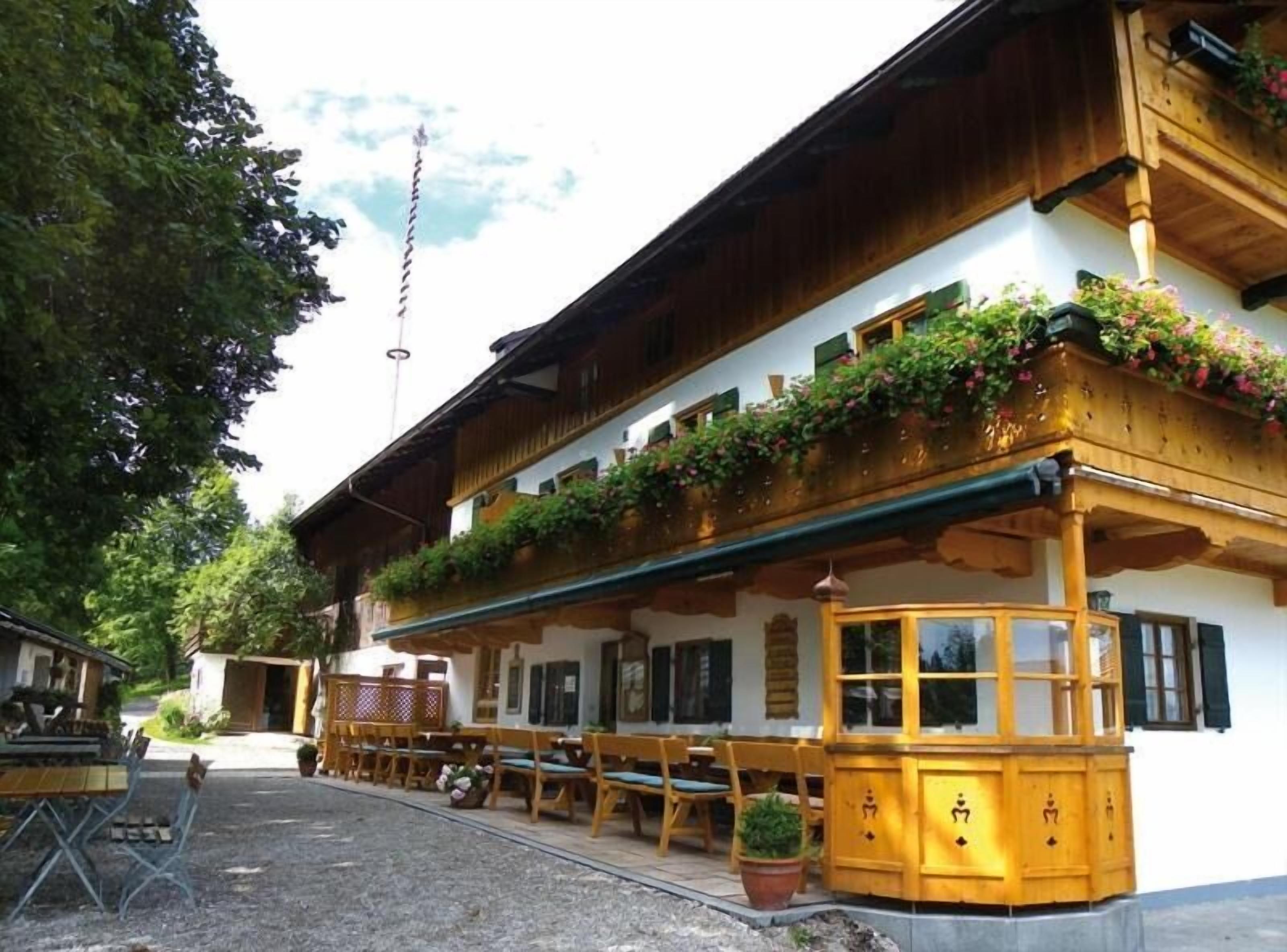 A traditional wooden building with a balcony adorned with flowers, outdoor seating, and a clear sky.