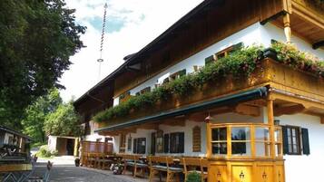 A traditional wooden building with a balcony adorned with flowers, outdoor seating, and a clear sky.