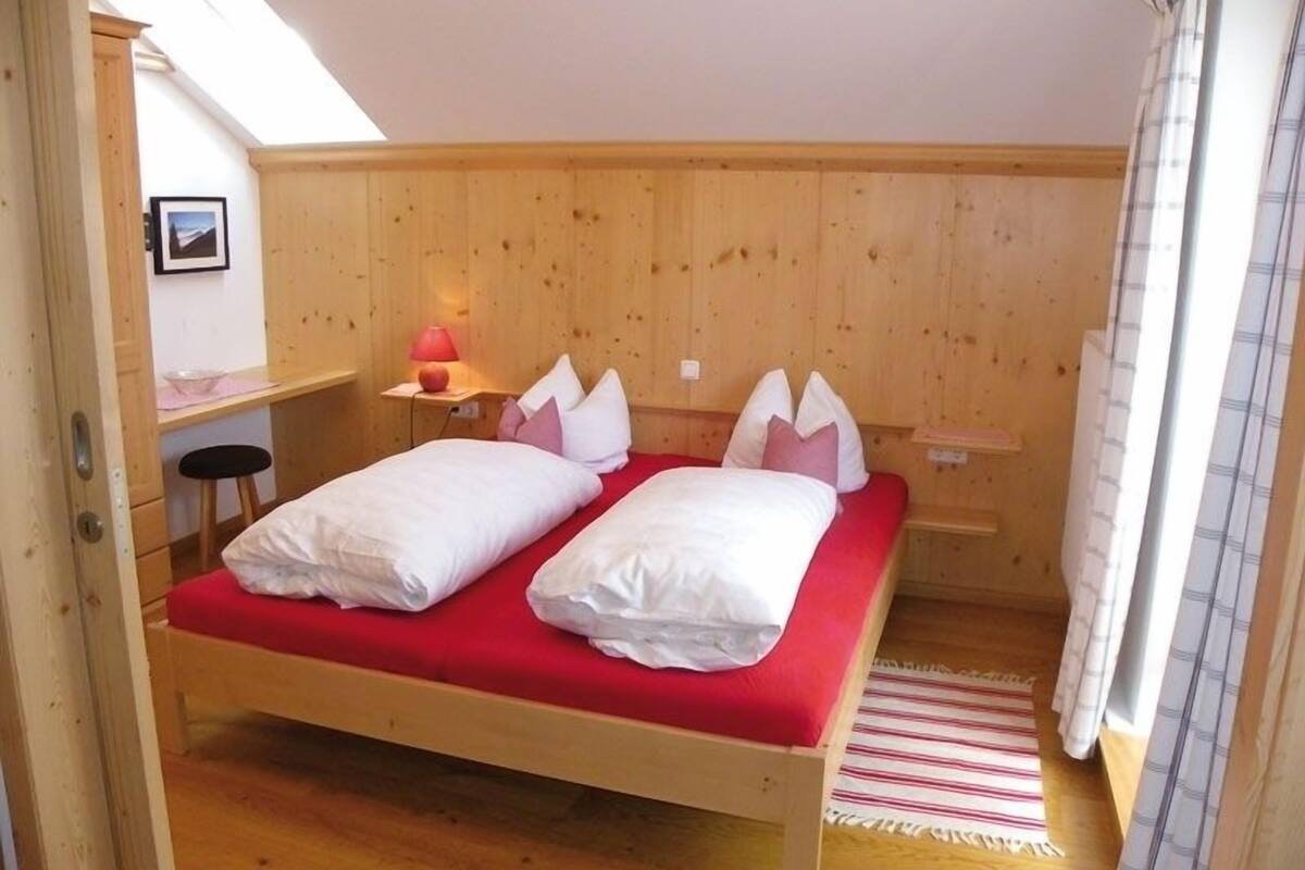 A single bed with a red mattress and white bedding in a room with wooden walls and a sloped ceiling.