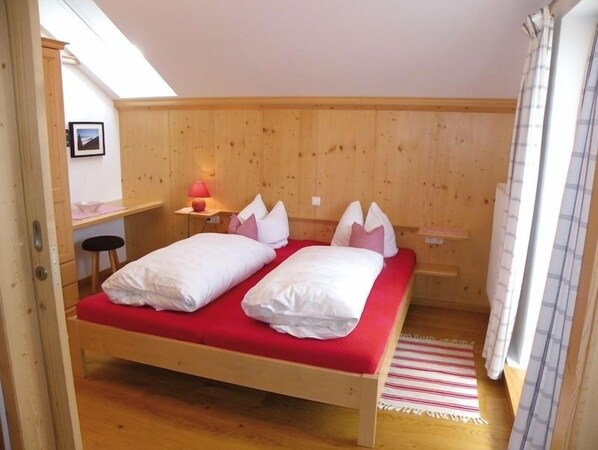 Una cama individual con colchón rojo y ropa de cama blanca en una habitación con paredes de madera y techo inclinado.