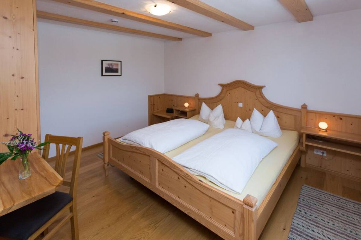 A wooden bed with white linens in a room with wooden beams and a small bedside table.
