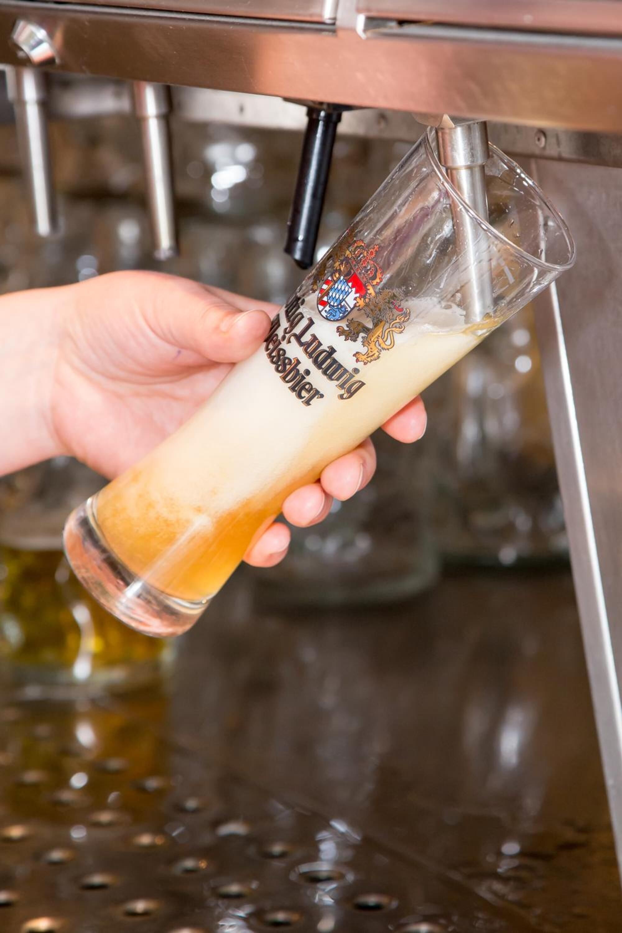 Eine Hand hält ein Glas mit einem Logo und Text, das unter einem Wasserhahn platziert ist.