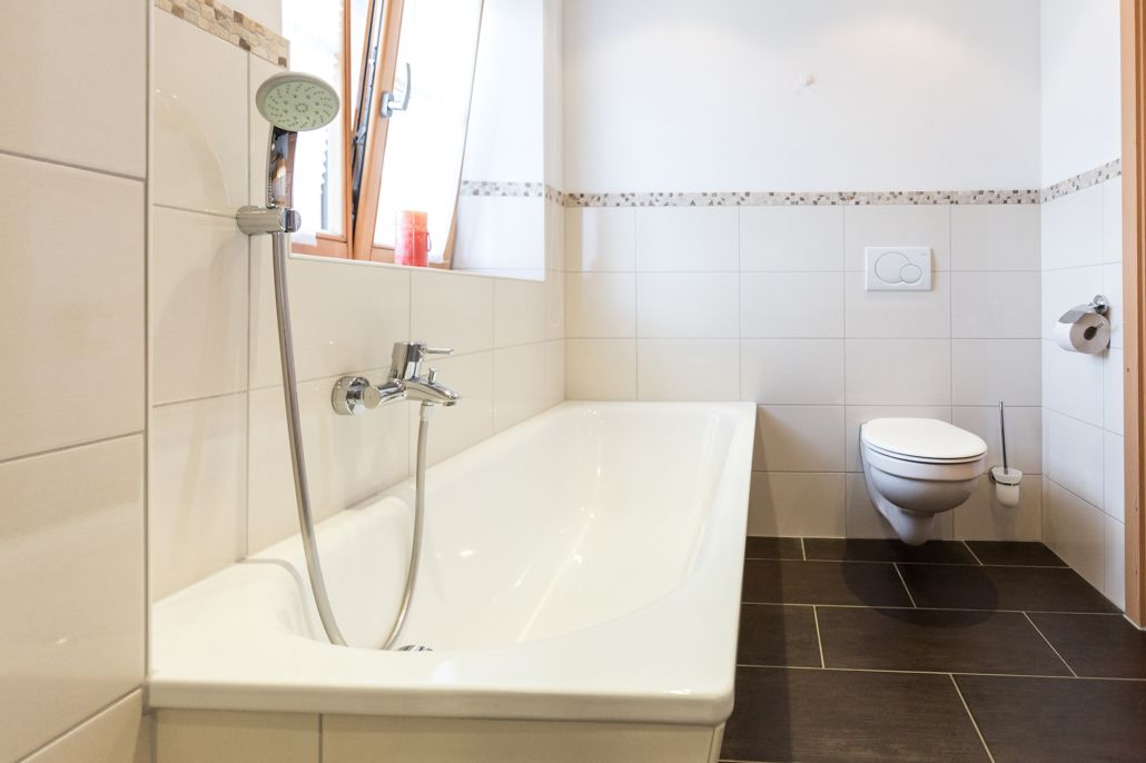 A bathroom with a white bathtub, a showerhead, a toilet, and a window.