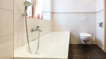 A bathroom with a white bathtub, a showerhead, a toilet, and a window.
