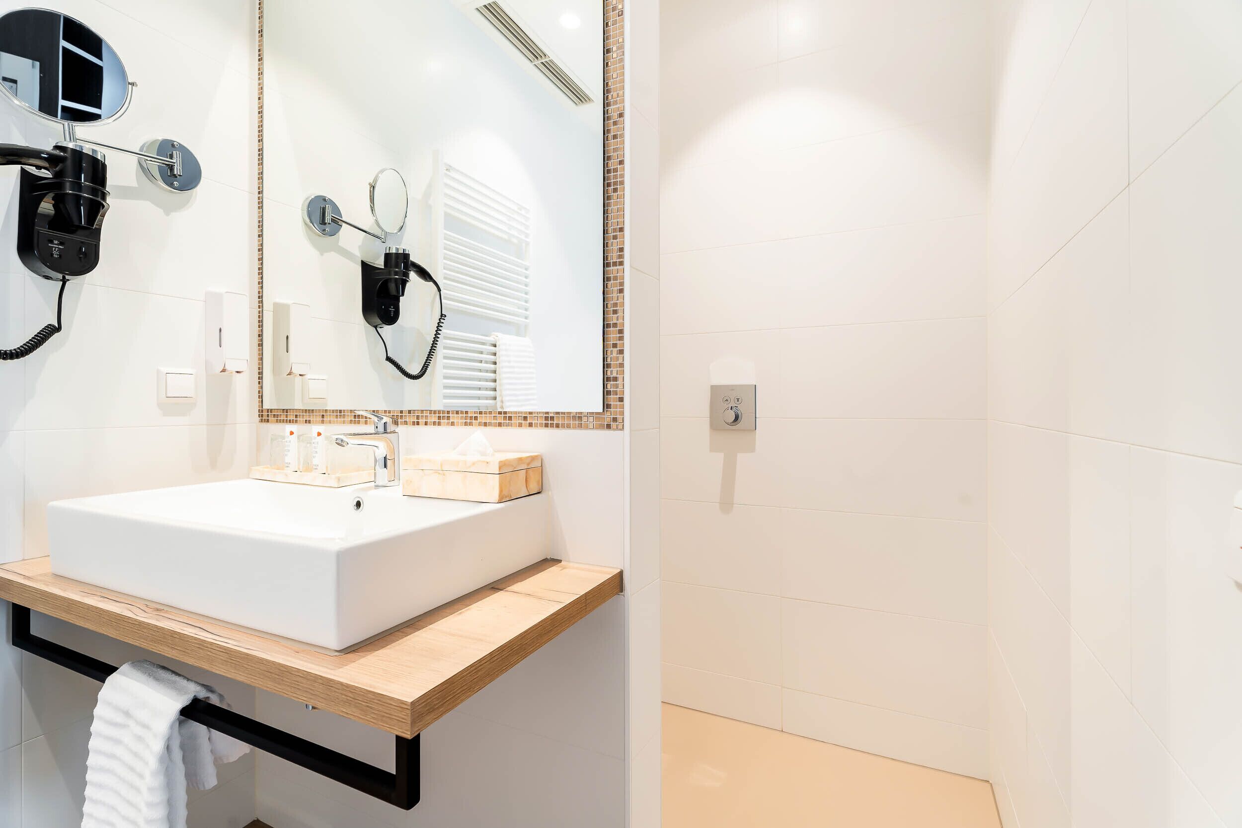 A modern bathroom with a white sink, a mirror, a hairdryer, and a towel rack.
