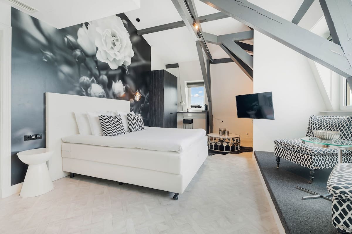 A modern bedroom with a large bed, a TV, and a unique ceiling structure.