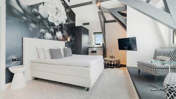 Une chambre à coucher moderne, dotée d’un grand lit, d’une télévision et d’une structure de plafond originale.