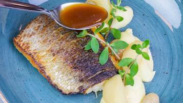 A plate with a piece of grilled fish, mashed potatoes, and a garnish of green leaves.