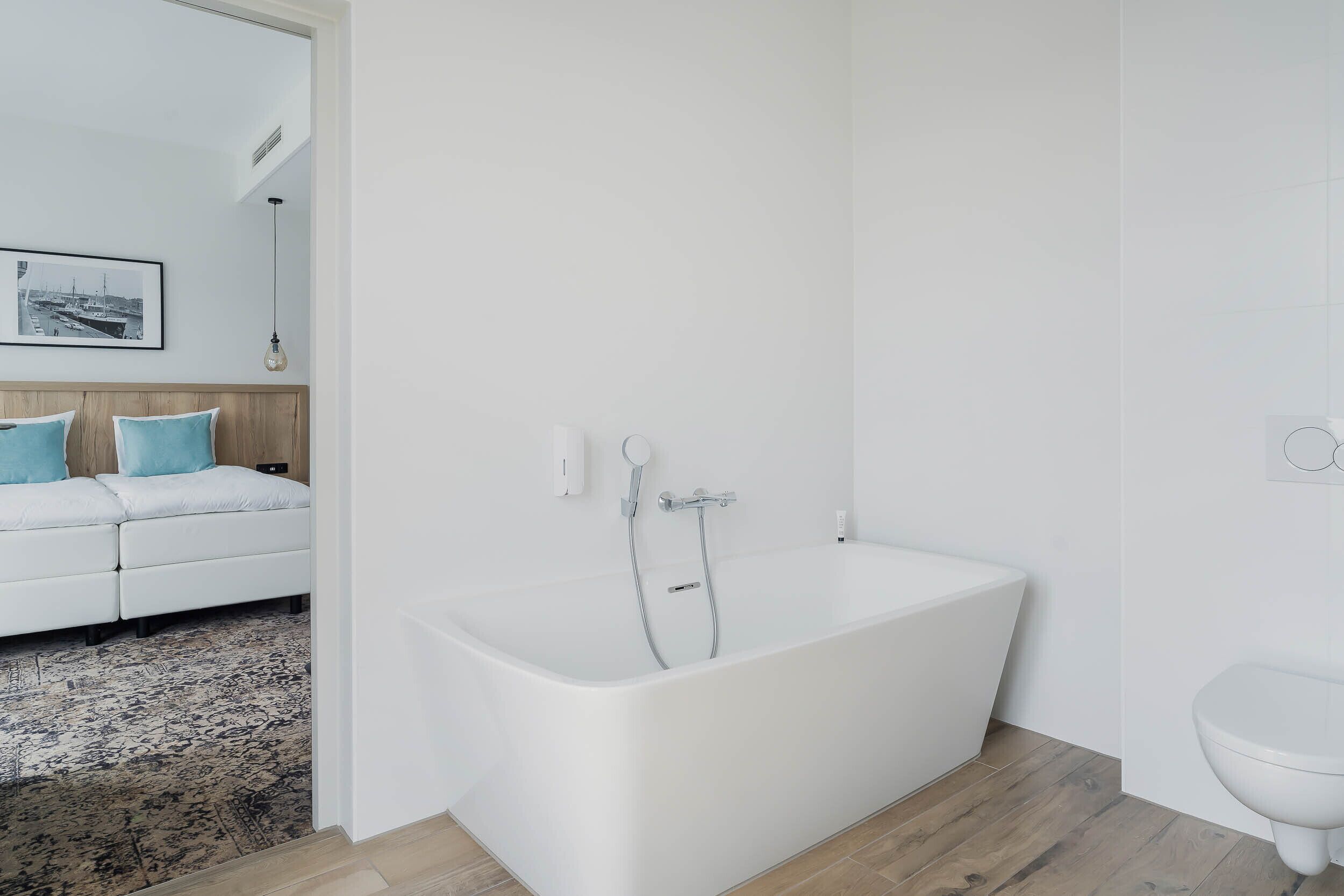 Un baño moderno con una bañera blanca, un inodoro blanco y suelo de madera.