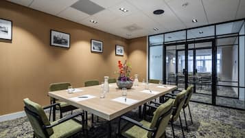 Une salle de conférence avec une longue table, des chaises, des tableaux encadrés accrochés au mur et une grande fenêtre.