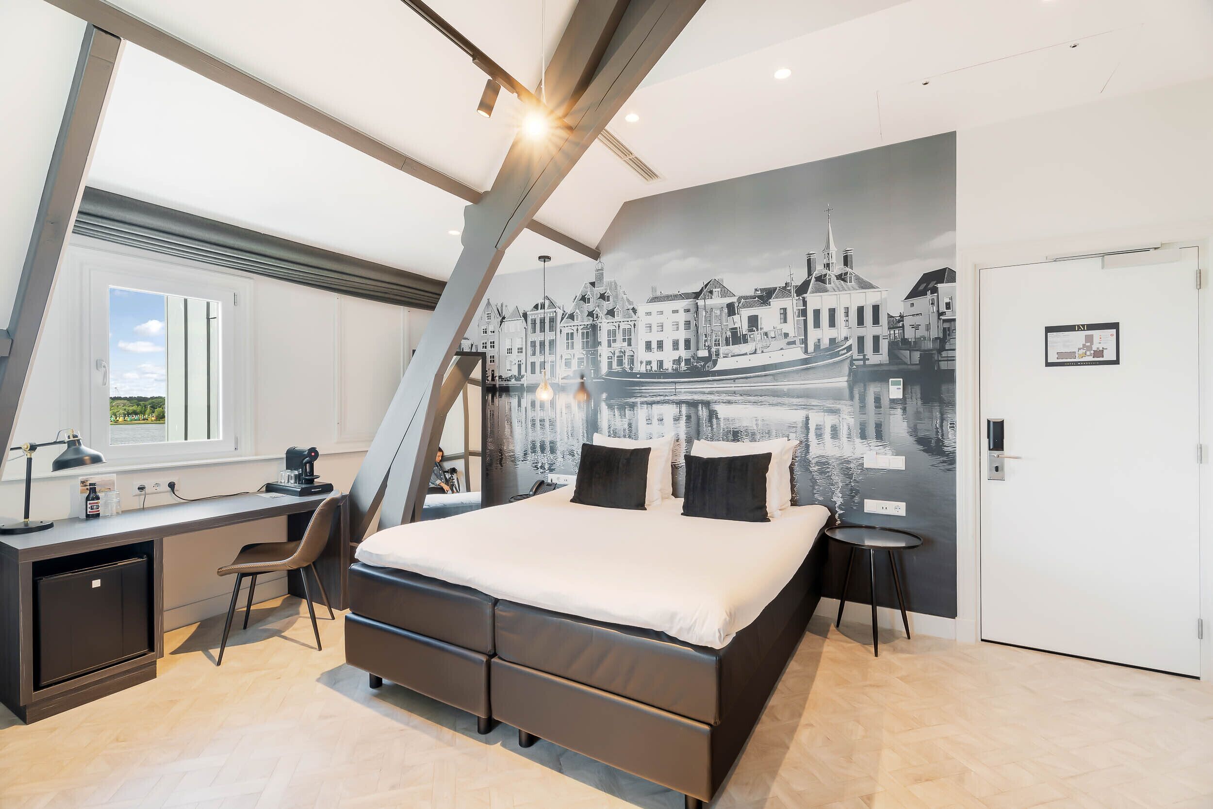 Un dormitorio moderno con cama, escritorio y silla, con un mural de paisaje urbano en la pared.