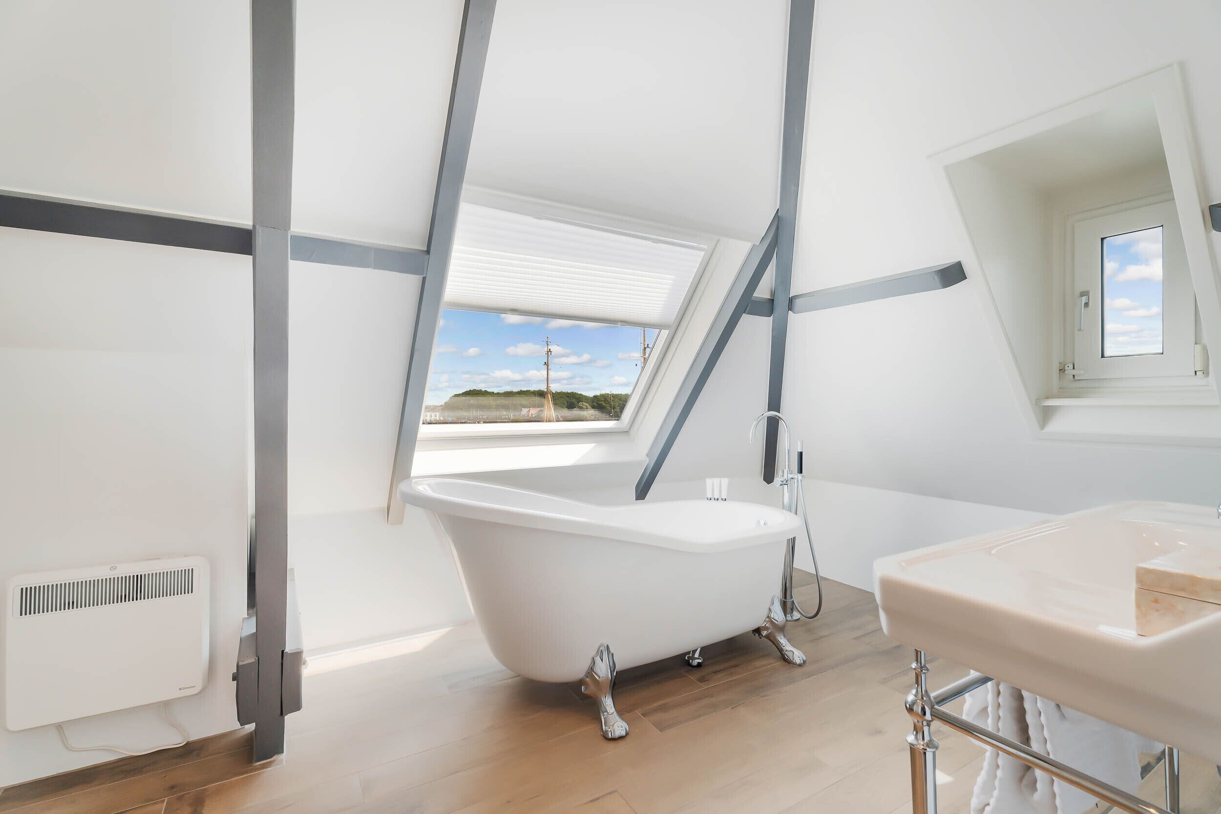 A modern bathroom with a freestanding bathtub, a vanity with a mirror, and a skylight providing natural light.