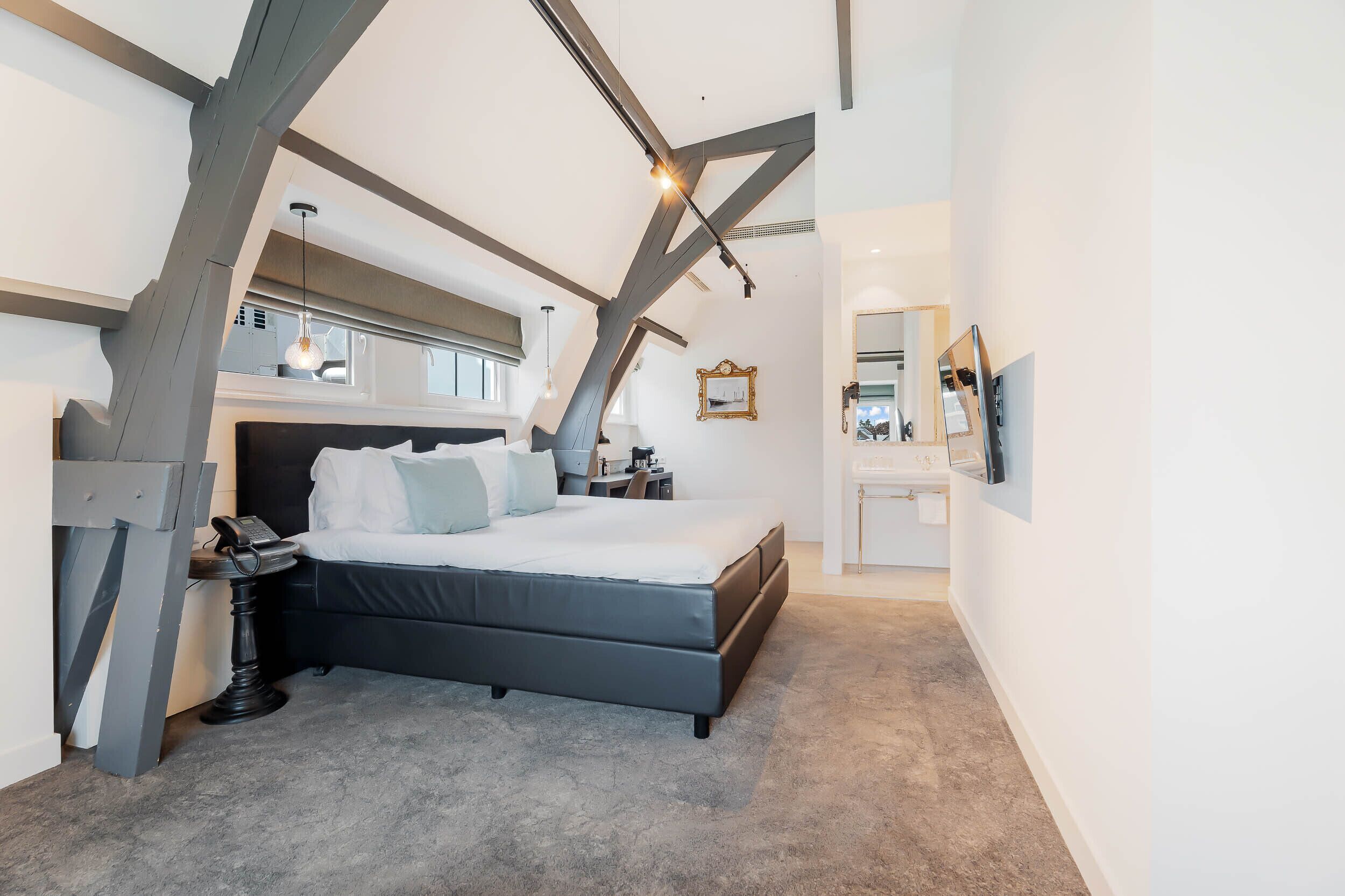A modern bedroom with a large bed, a desk, and a small table. There is a window with a view of the outside.