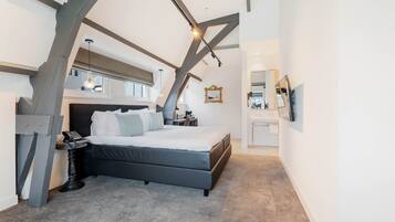 A modern bedroom with a large bed, a desk, and a small table. There is a window with a view of the outside.