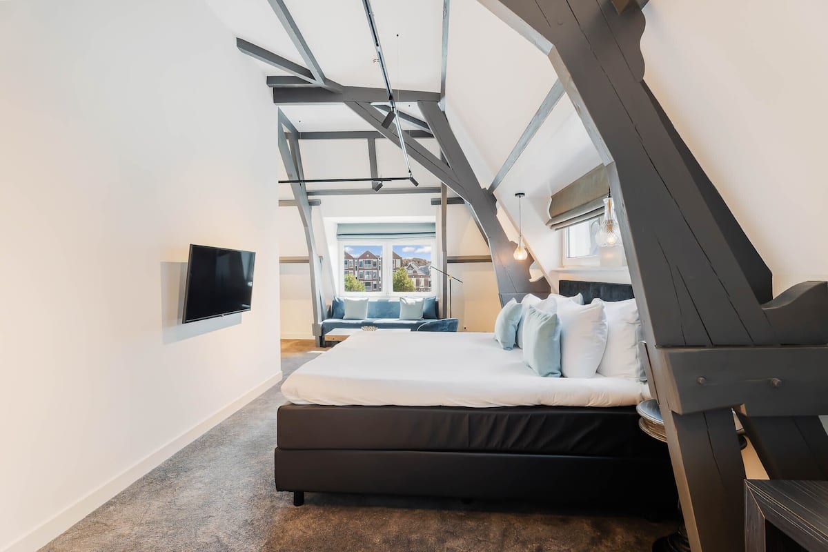 A modern bedroom with a large bed, a TV mounted on the wall, and a view of the outside.