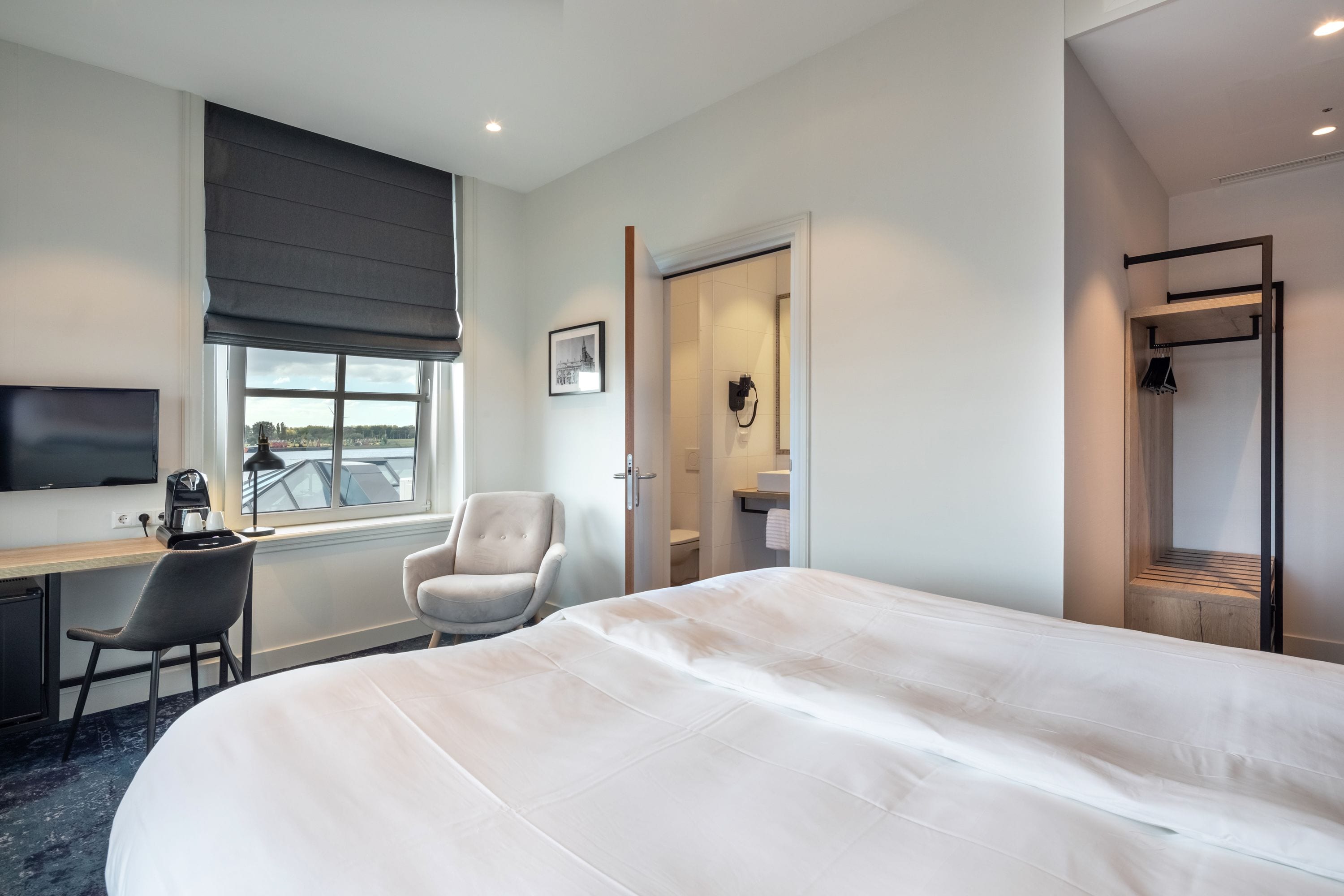 A hotel room with a large bed, a desk with a chair, a television, and a window with a view of the city.
