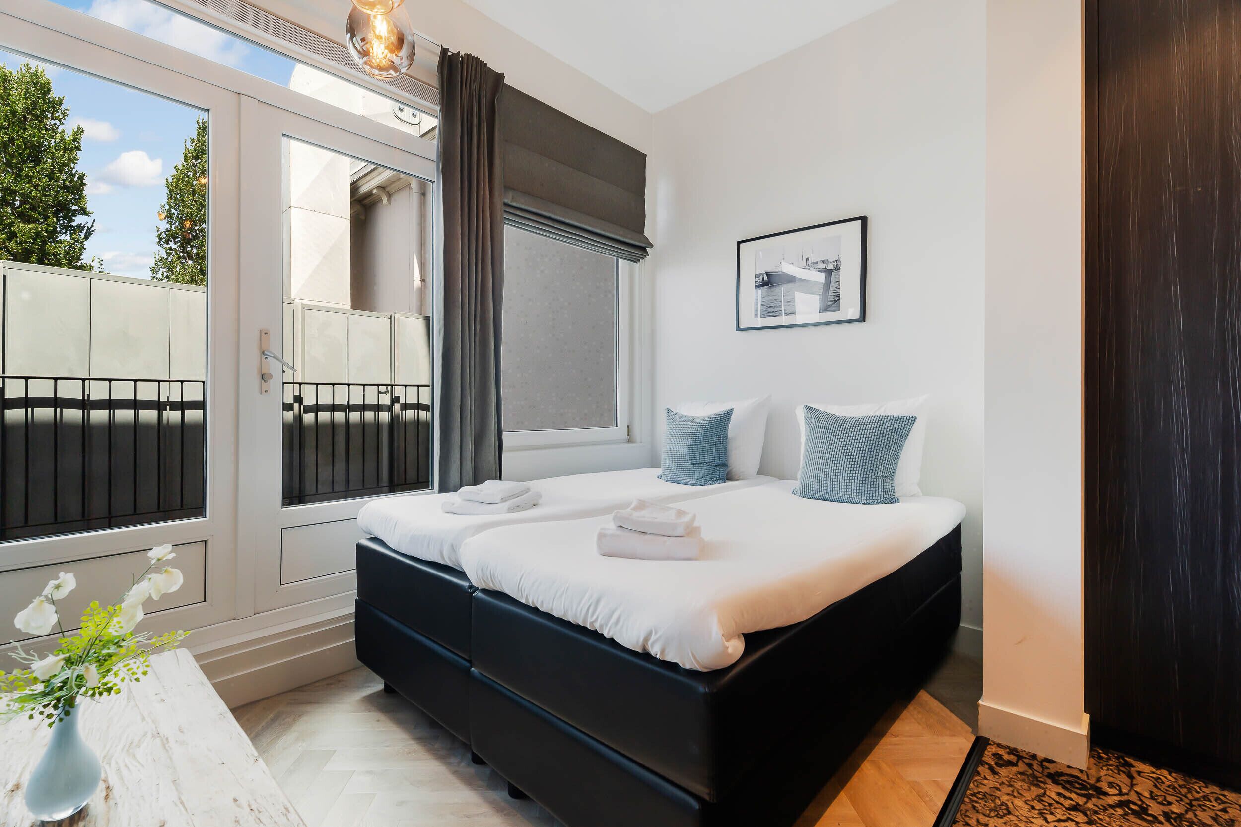 Een moderne slaapkamer met een groot bed, uitzicht door een schuifdeur en een ingelijste foto aan de muur.