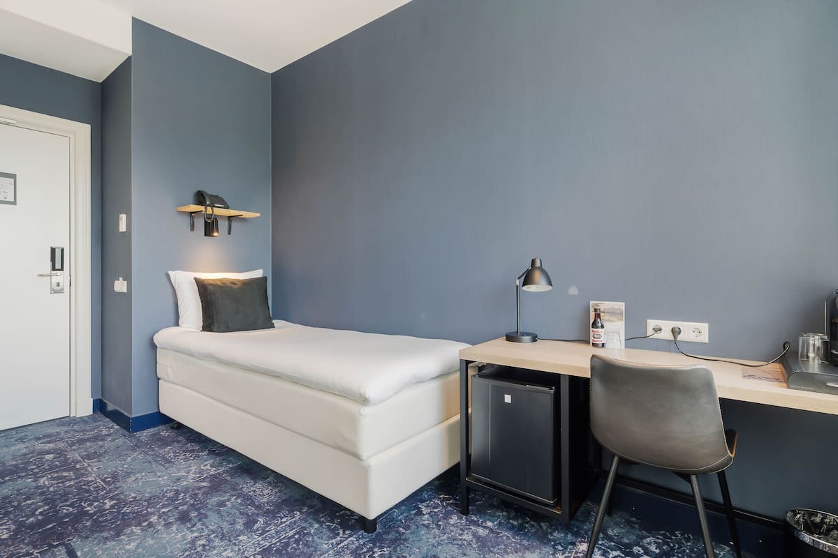A compact room with a bed, a desk, a chair, and a small refrigerator.