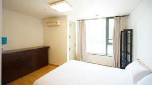 Une chambre à coucher comprenant un lit, une commode, une fenêtre avec des rideaux et un appareil de climatisation.