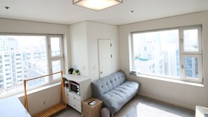 Un apartamento moderno con ventanas amplias, un sofá gris, una escalera de madera y una puerta blanca.