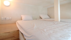 Una cama individual con ropa de cama blanca en una habitación con suelo de madera y paredes blancas.