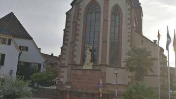 Eine Kirche mit einem hohen Kirchturm, einer Statue davor, Kopfsteinpflaster und eine Palmenbaum.