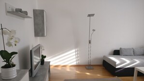 Ein modernes Wohnzimmer mit einer Couch, einem Couchtisch, einer Stehlampe, einem Fernseher und einer Topforchidee.