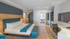 A modern hotel room with a large bed, a desk with a chair, a TV, and a walk-in closet.
