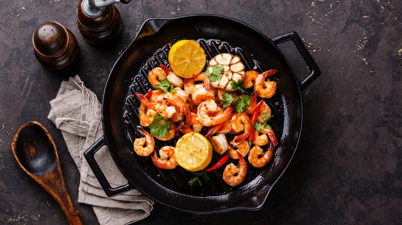 Una sartén con camarones a la parrilla, limón y hierbas.
