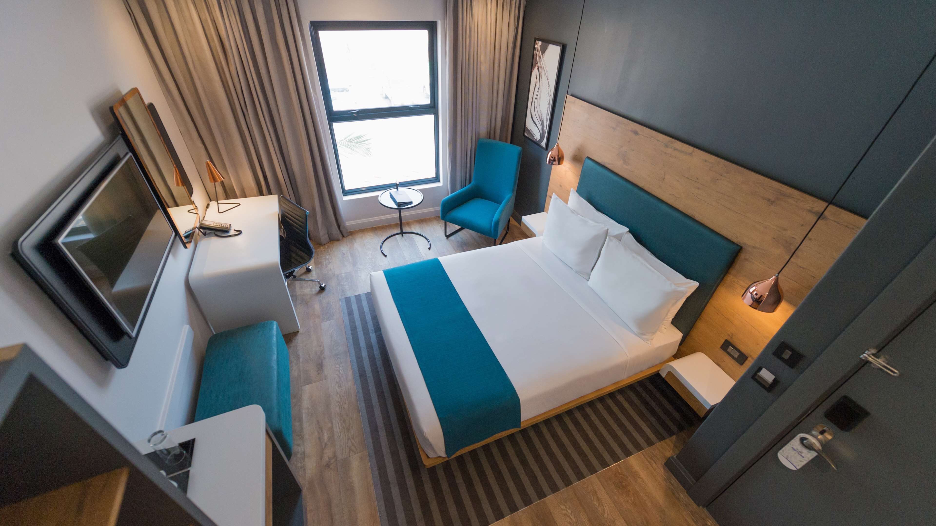 Ein Hotelzimmer mit einem großen Bett, einem Schreibtisch mit Fernseher, einem Sessel und einem kleinen Tisch.