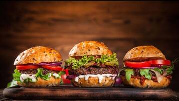 Three burgers on a wooden board against a wooden background.
