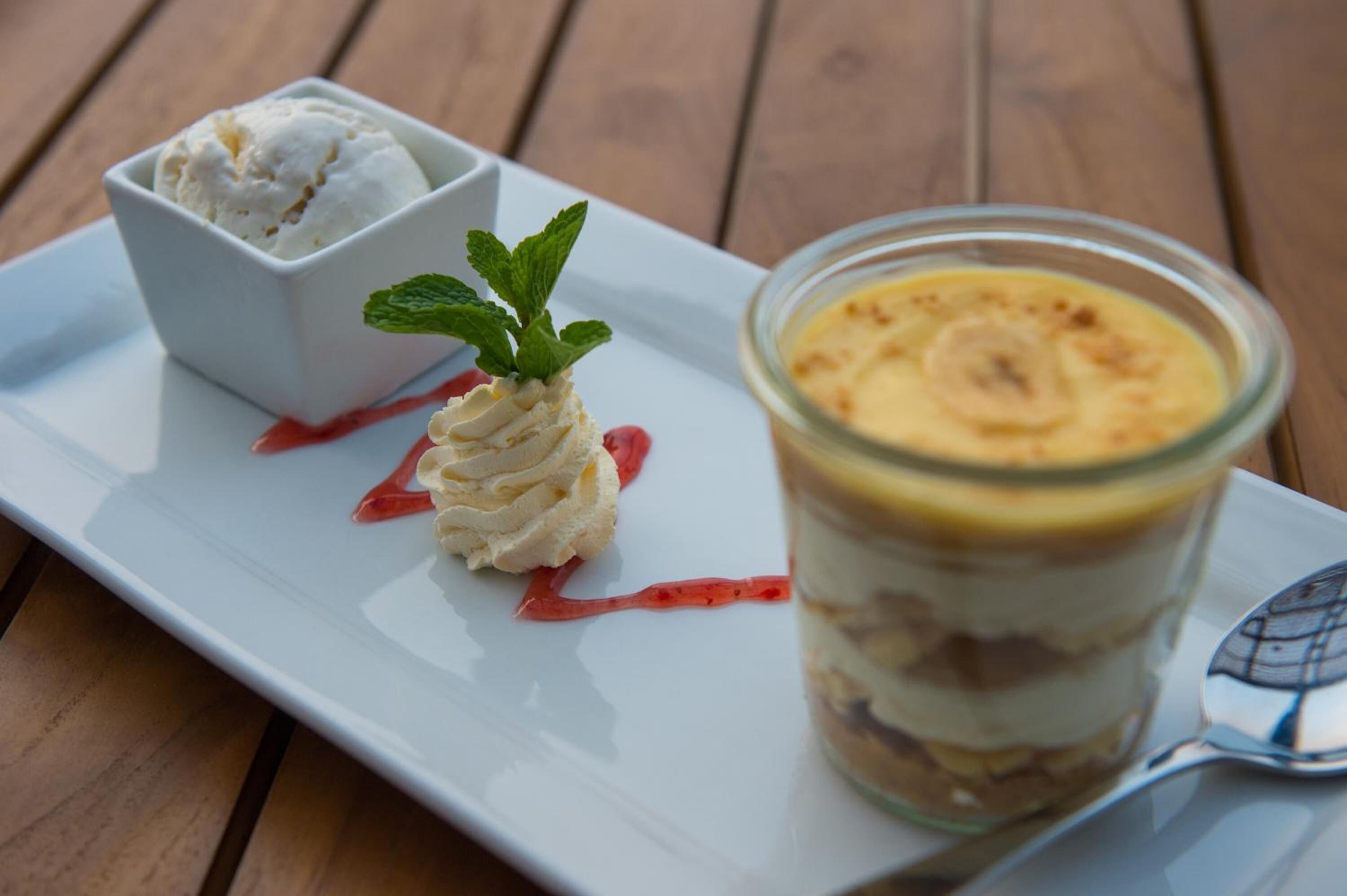 A dessert plate with a scoop of ice cream, a dollop of whipped cream, and a glass of layered dessert with a mint garnish.