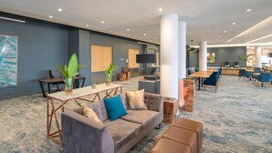 A modern lounge area with a sofa, coffee table, and chairs, a reception desk, and a large painting on the wall.