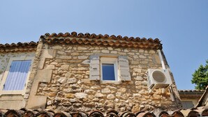 A stone building with a tiled roof, two windows with shutters, and an air conditioning unit. - Au Mazet de Carmélina, an old building dating from 1850 in the heart of the Alpilles mountains (Paradou)