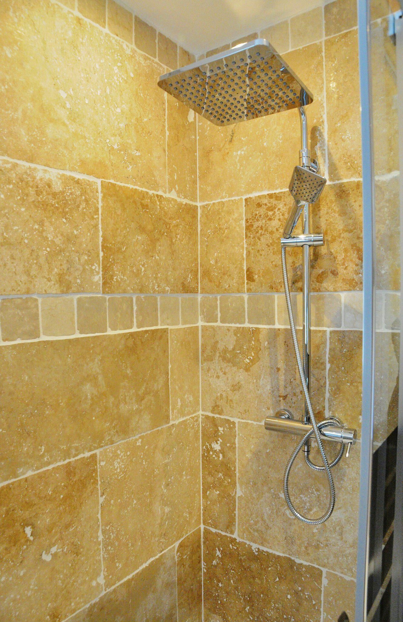 A shower with a handheld showerhead and a wall-mounted control valve.